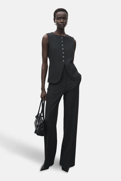 Blazer gris sans manches de MANGO avec six boutons devant, porté avec un pantalon et un sac noir.