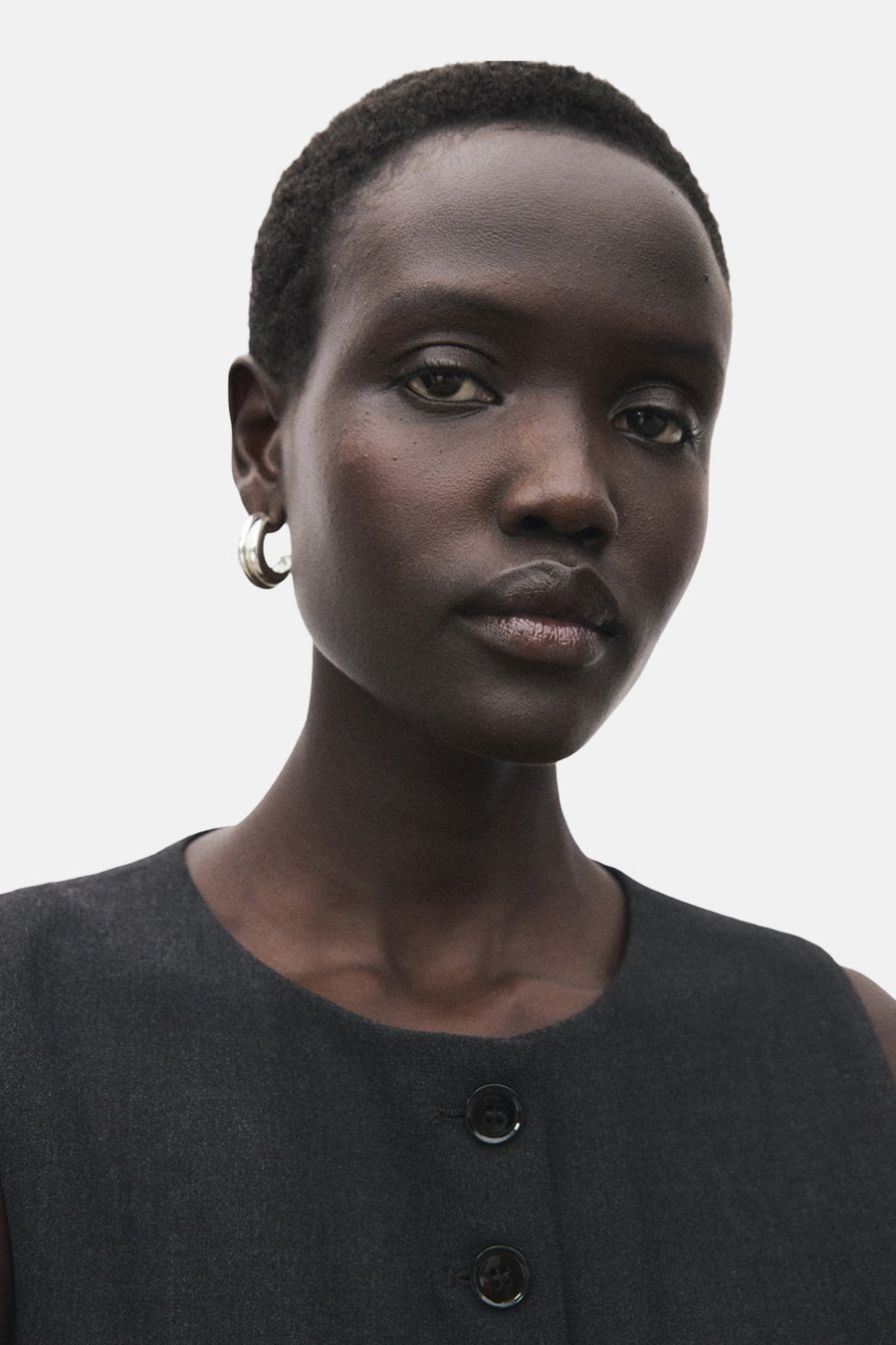 Blazer gris van MANGO, fermé par deux boutons, porté avec des boucles d'oreilles argentées.
