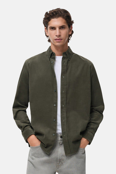 Chemise à manches longues verte de MANGO, portée ouverte sur un t-shirt blanc, avec un pantalon gris.