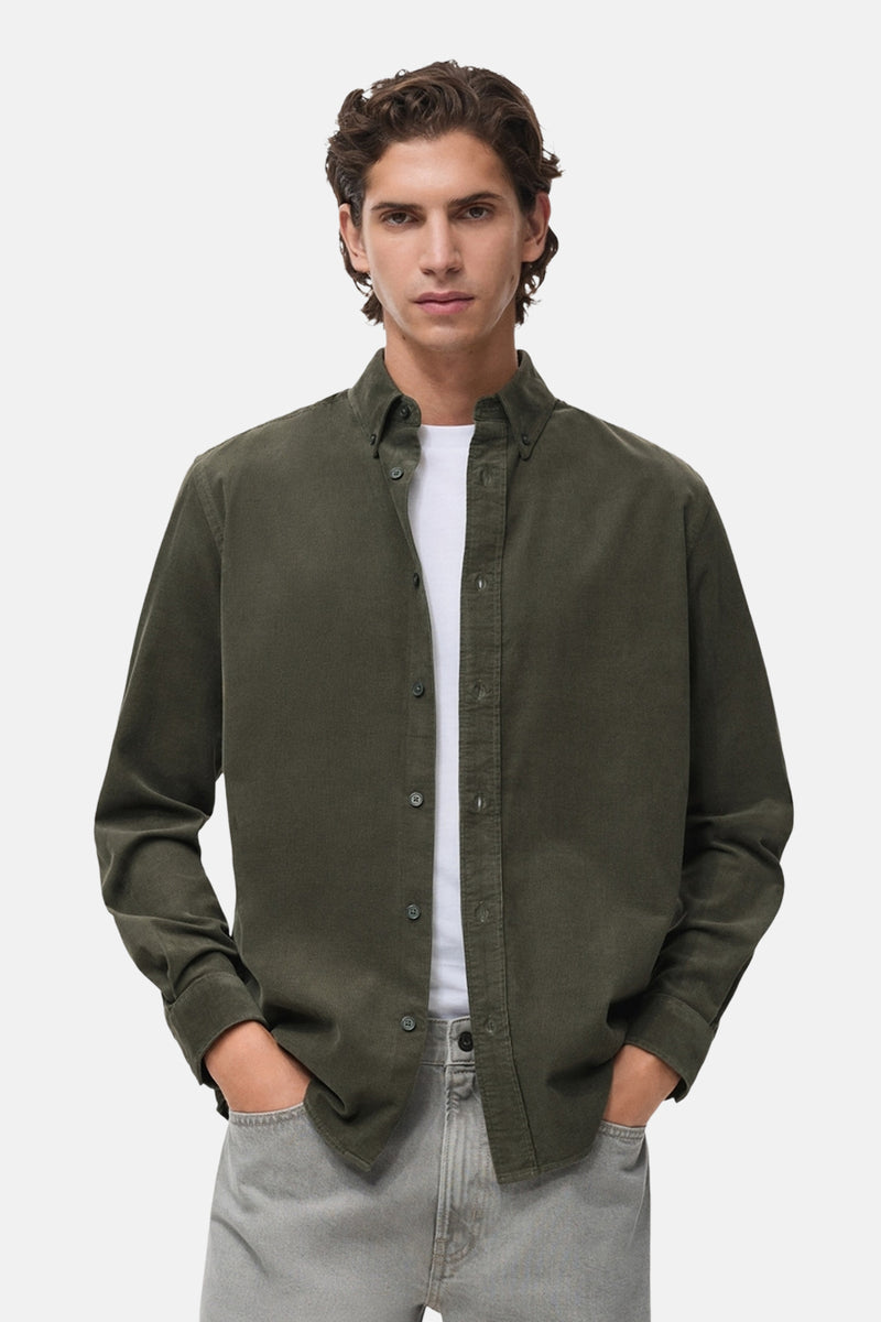 Chemise à manches longues verte de MANGO, portée ouverte sur un t-shirt blanc, avec un pantalon gris.