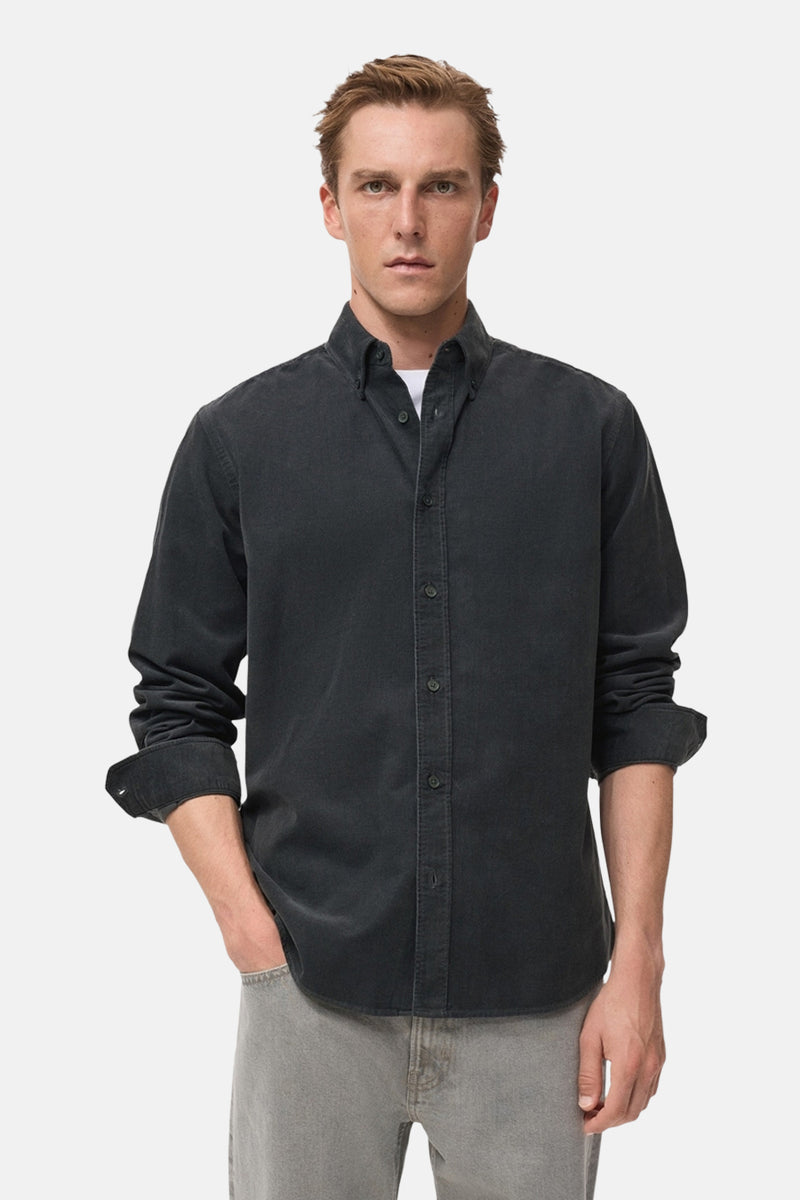 Chemise à manches longues grise de MANGO, portée avec un t-shirt blanc et un pantalon gris.