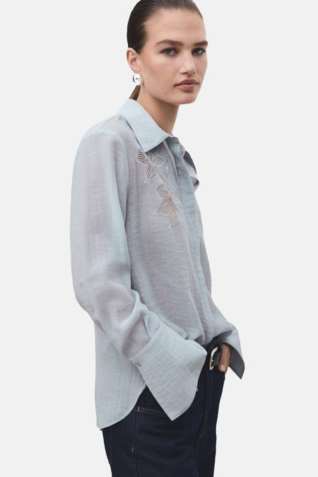 Blauwe blouse met lange mouwen van MANGO, gedragen met een wijde jeans en zwarte pumps, van achteren gezien.