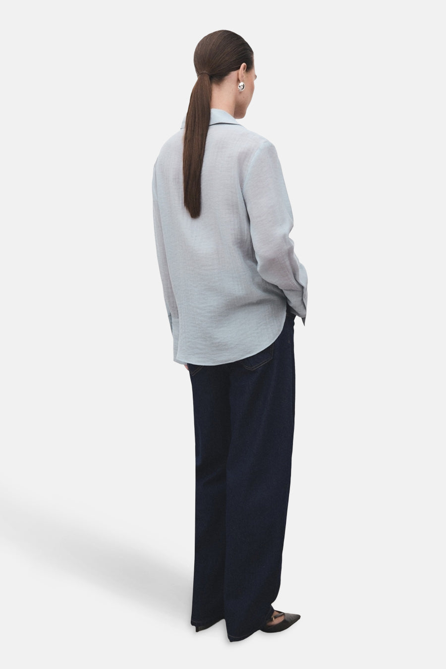 Chemise à manches longues bleue de MANGO, portée avec un jean ample et des escarpins noirs, vue de dos.

