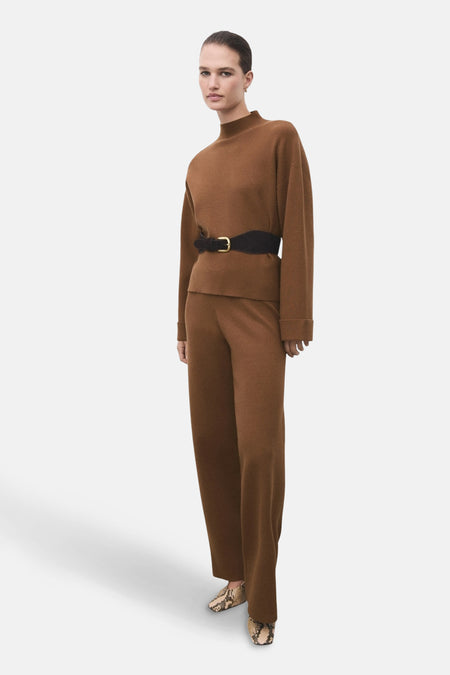 Pull à col roulé brun de MANGO, porté avec une ceinture noire et un pantalon marron assorti, chaussures à motifs peau de serpent.
