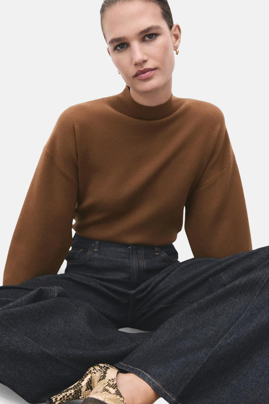 Pull à col roulé marron de MANGO, porté avec un pantalon en denim bleu foncé et des chaussures à motifs serpent.