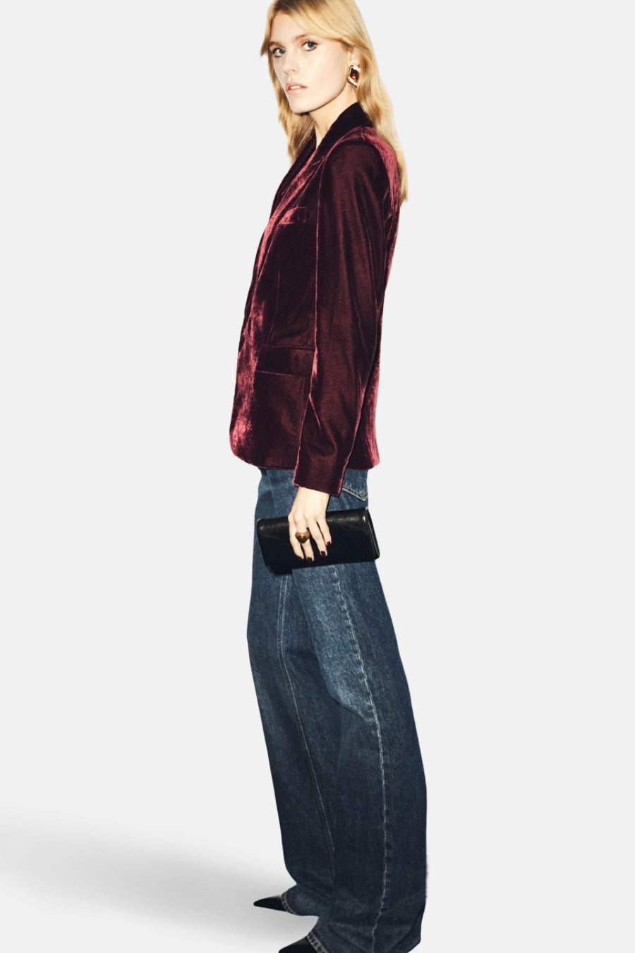 Blazer bordeaux en velours de MANGO, porté avec un jean ample bleu et une pochette noire.