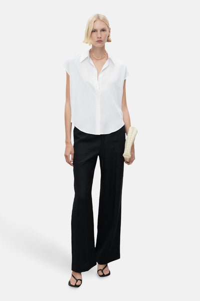 Chemisier blanc sans manches de MANGO, porté avec un pantalon noir large et des sandales.