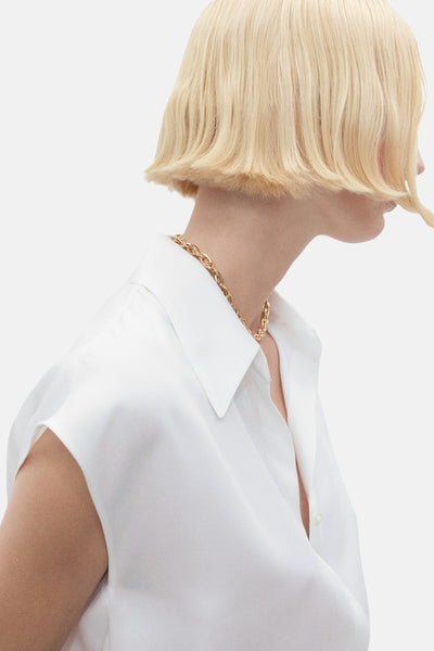 Wit mouwloos overhemd van MANGO, gedragen met een gouden ketting en kort blond kapsel.