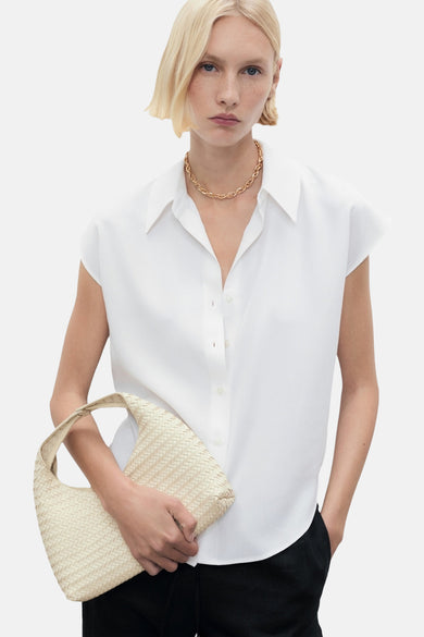 Chemisier blanc sans manches de MANGO, porté avec un collier doré et un sac tressé.

