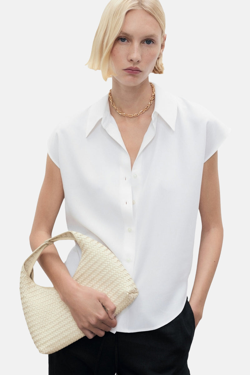 Chemisier blanc sans manches de MANGO, porté avec un collier doré et un sac tressé.
