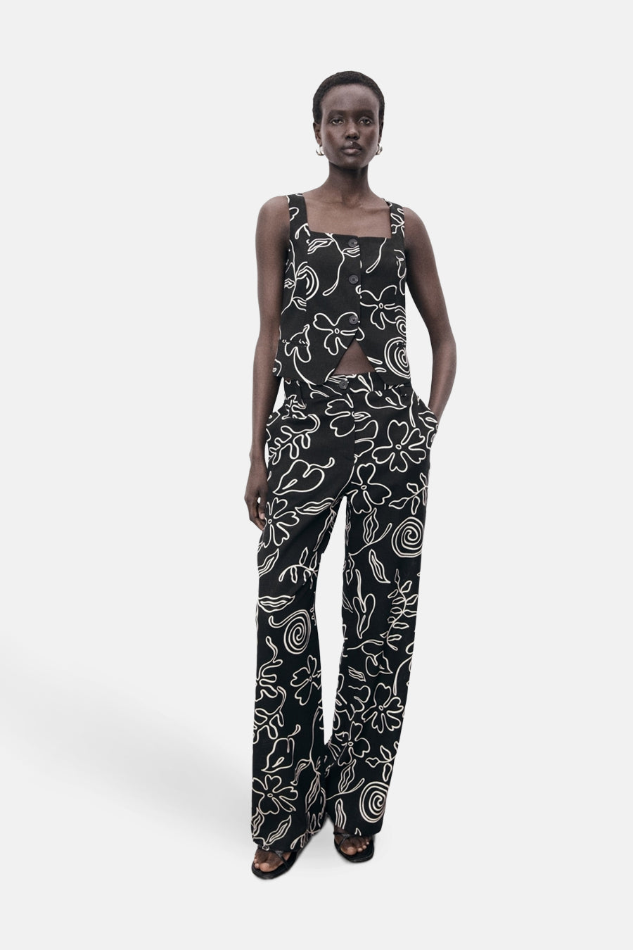 Zwart mouwloos bloesje van MANGO, met wit bloemenpatroon, gedragen met een bijpassende broek.