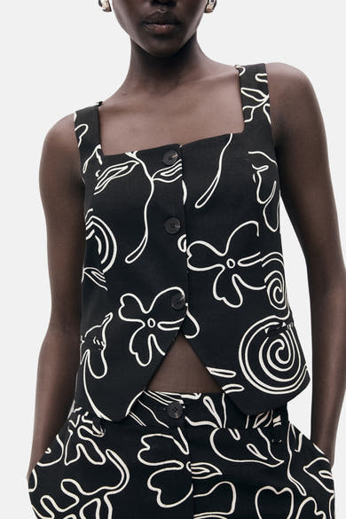 Zwarte mouwloze blouse van MANGO, met witte bloemenprint en korte pasvorm.