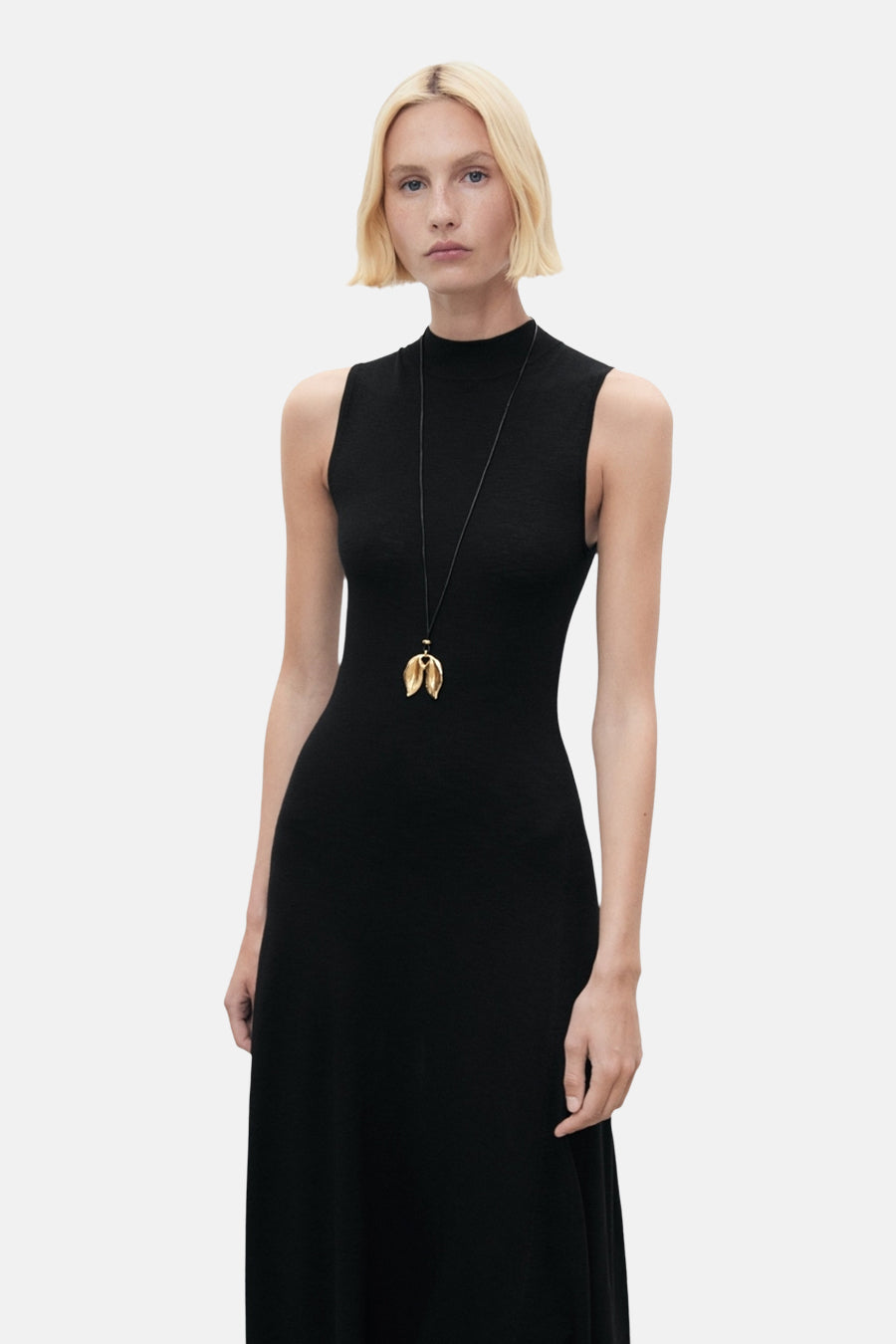 Zwarte nauwsluitende jurk van MANGO, met een gouden hangerketting.