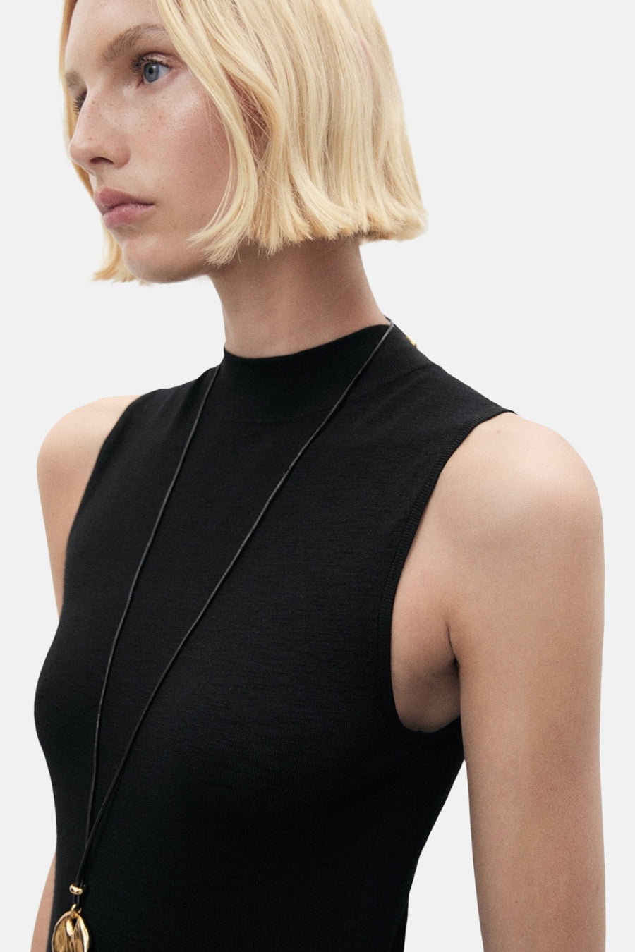 Zwarte nauwsluitende jurk van MANGO, met een gouden ketting en een col.