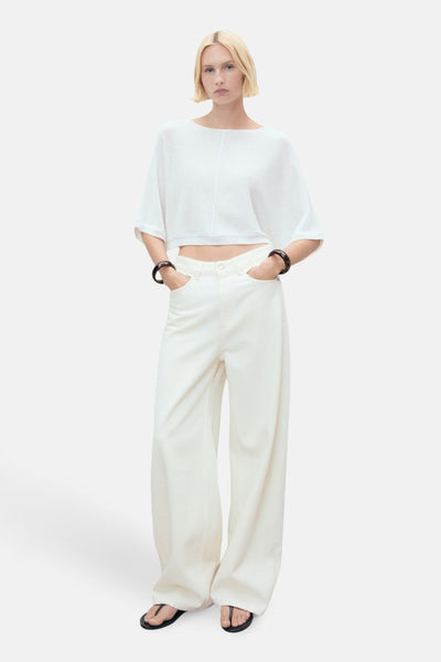 Witte rondehals trui van MANGO, gedragen met een witte broek met hoge taille en donkere armbanden.