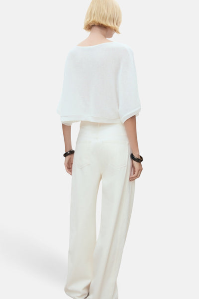 Witte rondehals trui van MANGO, korte mouwen, gedragen met een broek met hoge taille en zwarte armbanden.