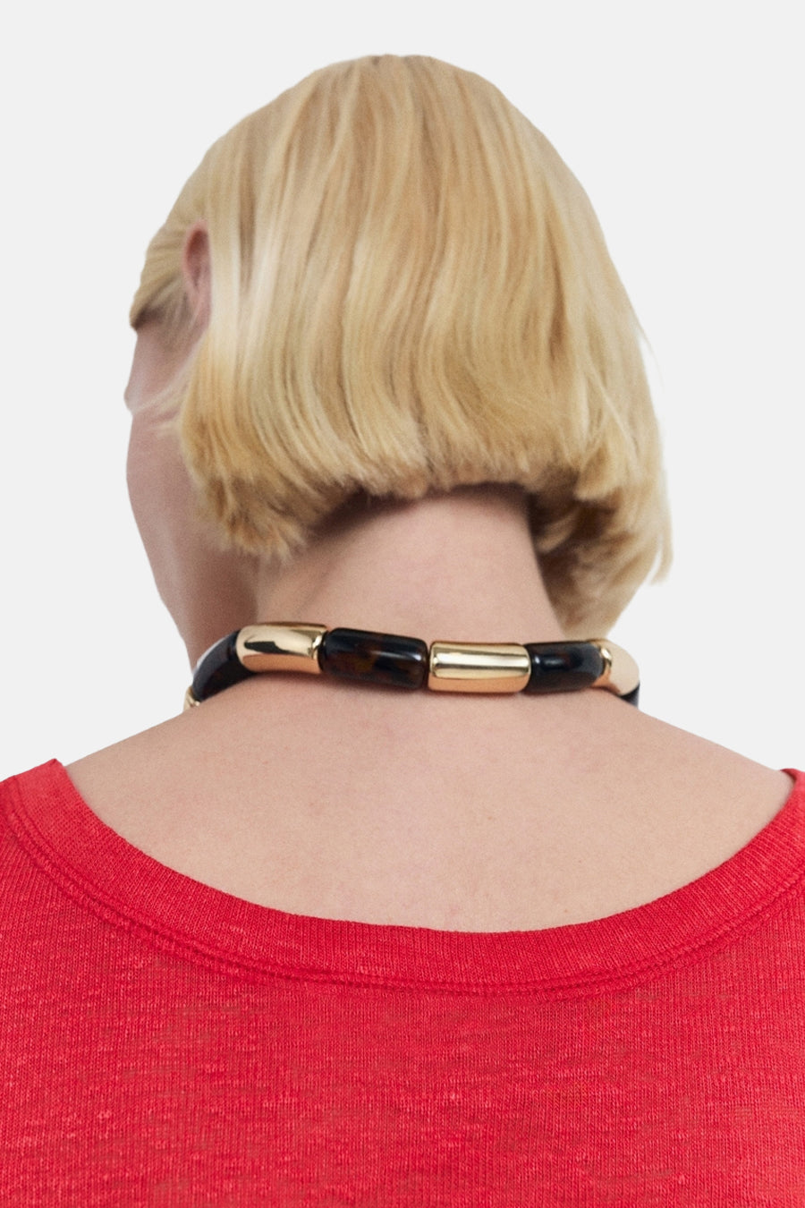 Rood mouwloos topje van MANGO, gedragen met een gouden en zwarte buisvormige ketting, op een witte achtergrond.