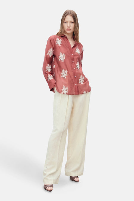 Bruin overhemd met lange mouwen van MANGO, versierd met witte bloemenpatronen, gedragen met een gebroken witte broek.