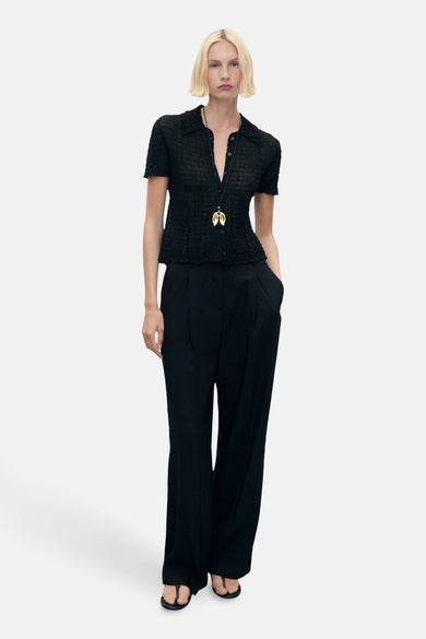 Zwarte broek van MANGO, wijd en geplooid, gedragen met een blouse en een hangerketting.