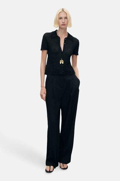 Zwarte broek van MANGO, wijd en geplooid, gedragen met een blouse en een hangerketting.