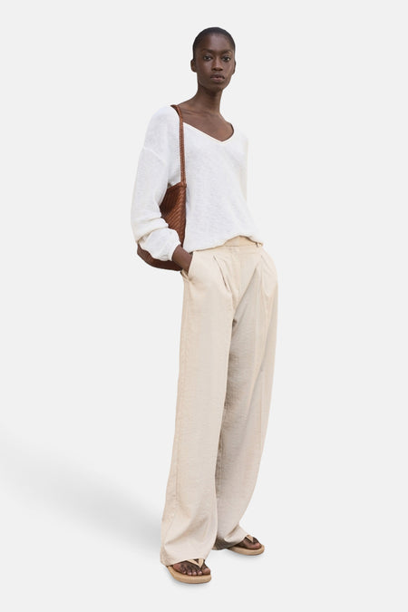 Beige broek van MANGO, wijd en met plooien, gedragen met een witte trui en bruine sandalen.