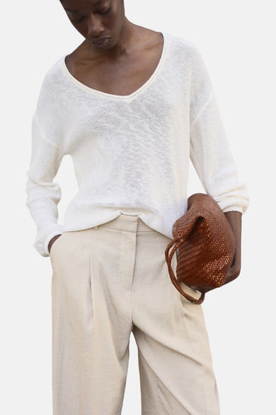 Beige broek van MANGO, losse pasvorm met plooien en subtiele textuur, gedragen met een trui en een gevlochten tas.