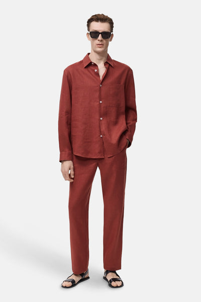 Chemise à manches longues rouge par MANGO, avec col et poche de poitrine, portée avec un pantalon assorti et des sandales.