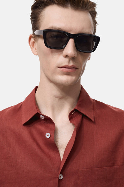 Chemise à manches longues rouge de MANGO, en lin texturé, portée ouverte avec des lunettes de soleil noires.
