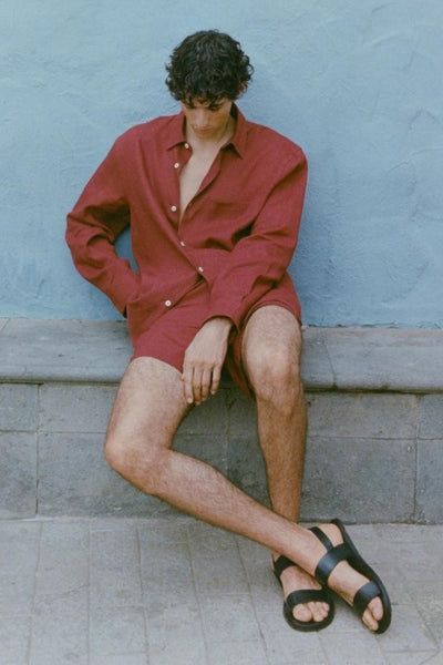 Chemise à manches longues rouge de MANGO, portée par un homme avec des shorts et des sandales.