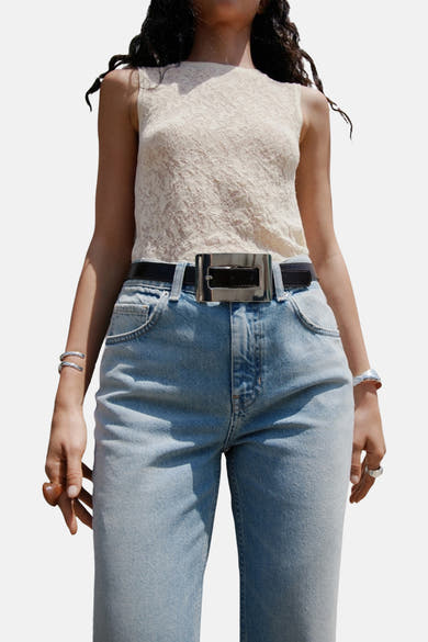 Jean évasé bleu clair de MANGO, porté avec un haut en dentelle et une ceinture noire à boucle argentée.