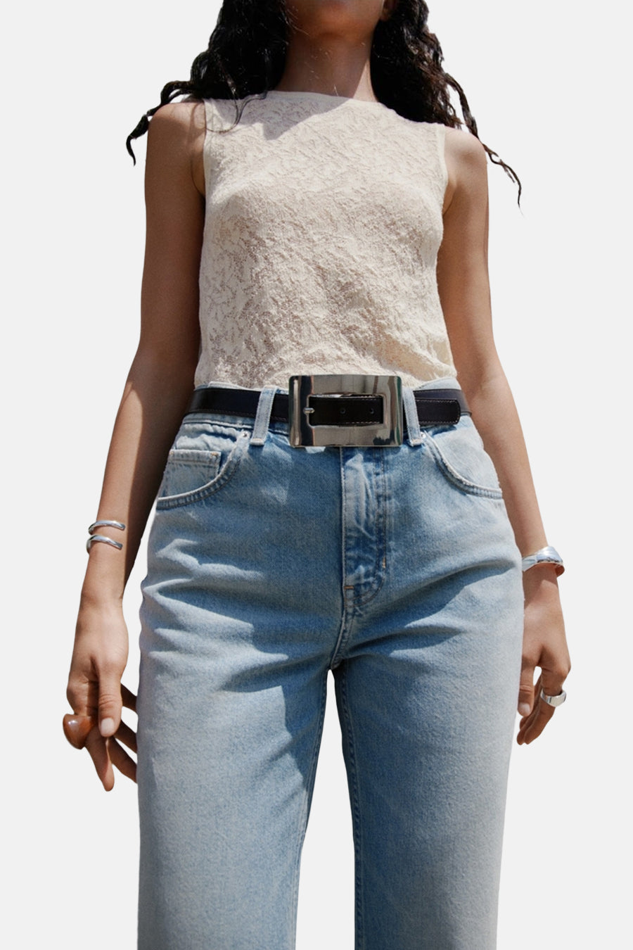 Jean évasé bleu clair de MANGO, porté avec un haut en dentelle et une ceinture noire à boucle argentée.