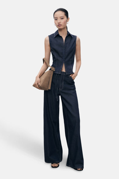Chemisier en denim bleu foncé sans manches de MANGO, porté avec un pantalon assorti, sac à main marron.