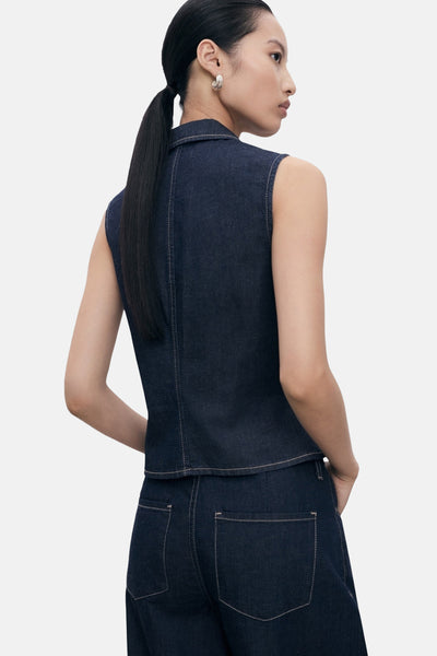 Chemisier sans manches en denim bleu foncé de MANGO, avec coutures apparentes et porté avec un pantalon assorti.