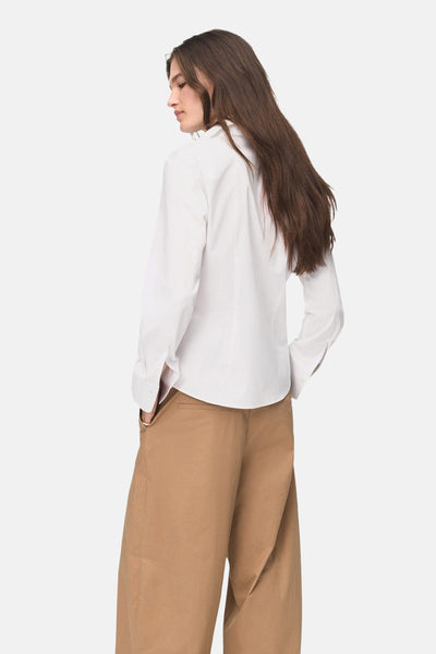 Chemisier blanc à manches longues de MANGO, porté avec un pantalon marron ample, vue de dos.
