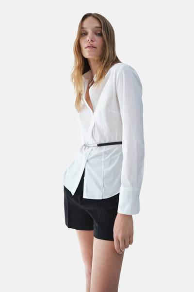 Wit overhemd met lange mouwen van MANGO, gedragen met een zwarte riem en een zwarte korte broek.
