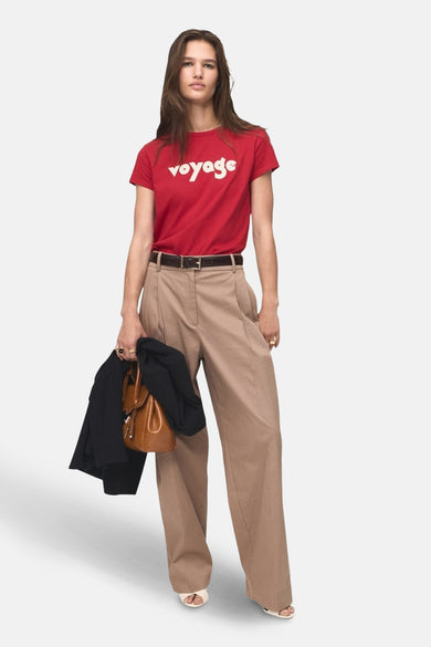 Rood T-shirt met korte mouwen van MANGO, met het woord "voyage" in het wit, gedragen met een beige broek en accessoires.