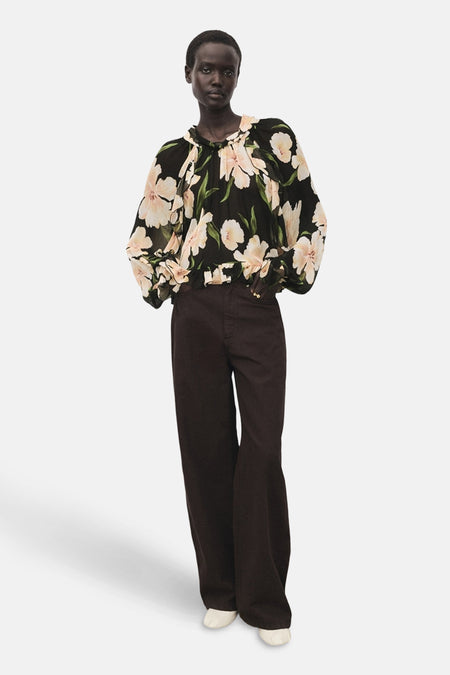 Chemisier à manches longues multicolore de MANGO, à motif floral sur fond noir, porté avec un pantalon marron.
