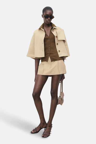Polo kaki à manches courtes de MANGO, porté avec une veste beige, un short et des sandales à talons.
