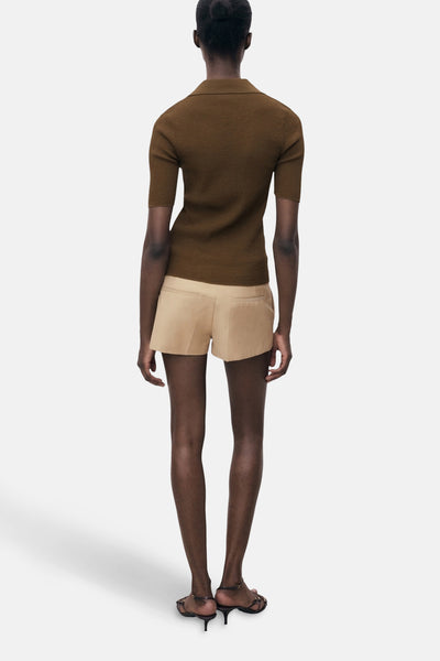 Polo kaki à manches courtes de MANGO, porté avec un short beige et des sandales à talons, vue de dos.

