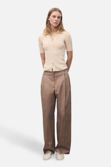 Polo beige à manches courtes de MANGO, porté avec un pantalon ample marron et des ballerines crème.