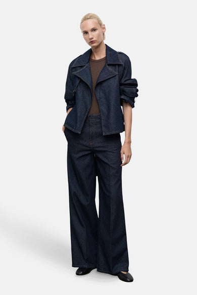 Veste courte en denim bleu foncé de MANGO, avec revers crantés et manches longues structurées, portée avec un t-shirt marron et un pantalon large.
