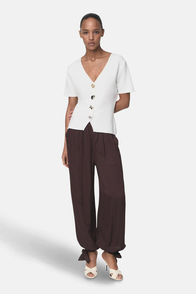 Cardigan blanc de MANGO, avec manches courtes et fermeture boutonnée asymétrique, porté avec un pantalon marron ample.