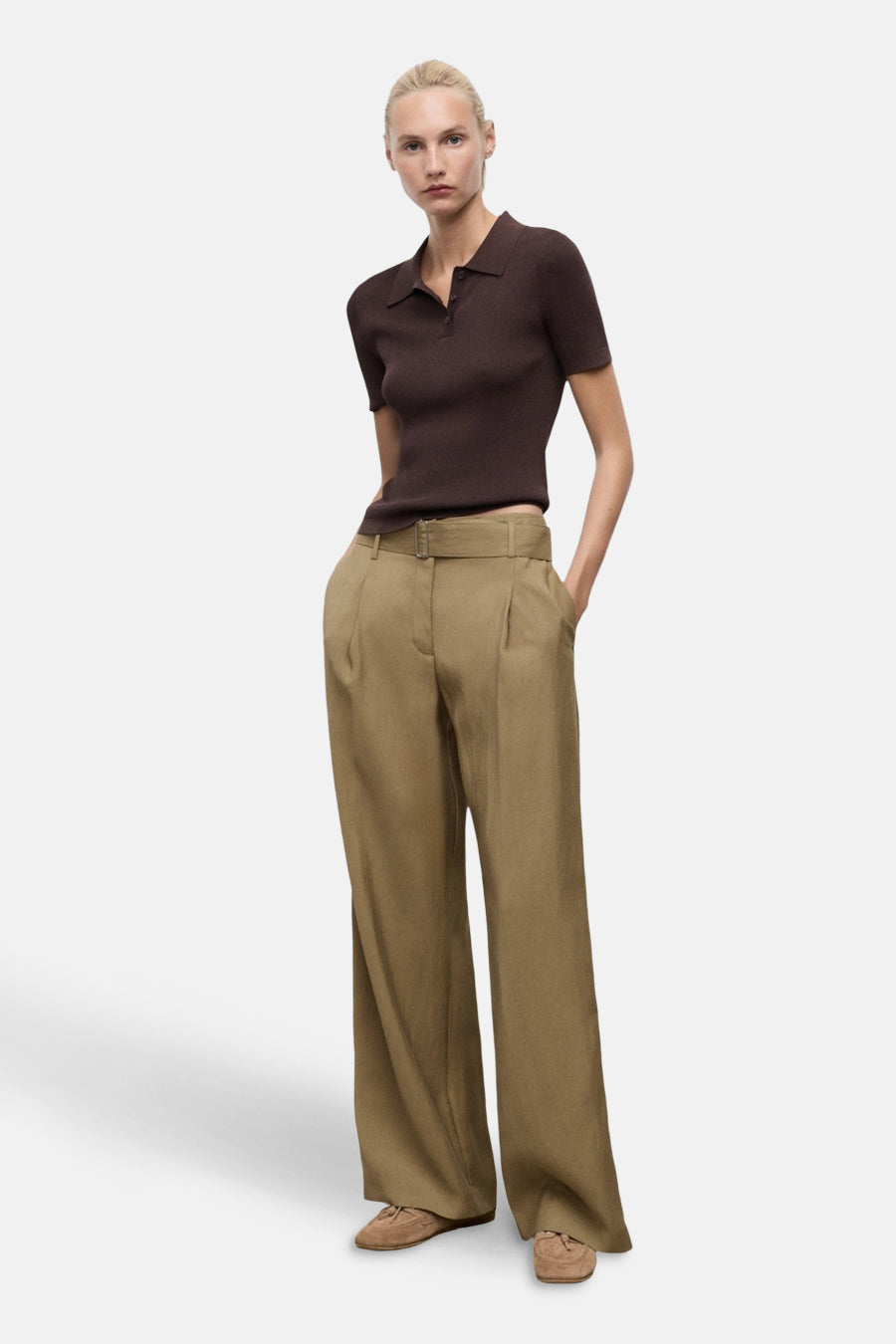 Pantalon kaki à jambes larges de MANGO, porté avec un haut polo marron et des chaussures plates en daim.
