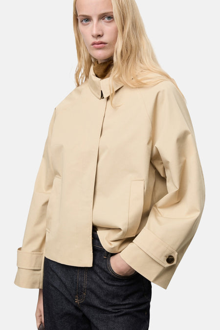 Korte beige jas van MANGO, met wijde mouwen en knoopdetails op de rug, gedragen met een donkere jeans.