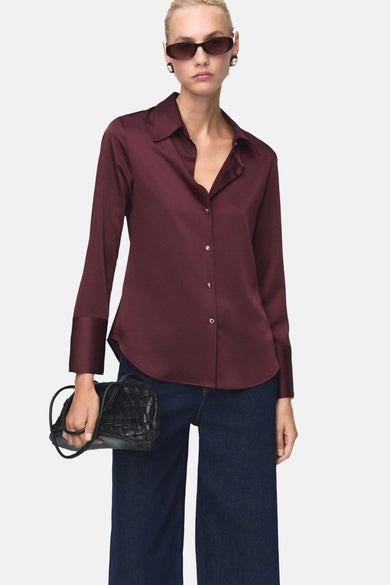 Bordeaux blouse met lange mouwen van MANGO, gedragen met een spijkerbroek en een zwarte gevlochten handtas.