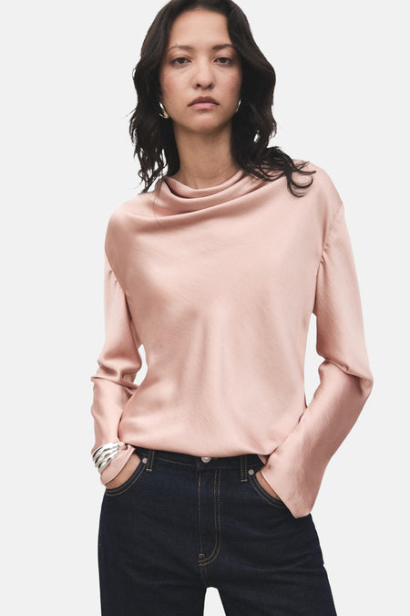 Roze blouse met lange mouwen van MANGO, met een gedrapeerde kraag, gedragen met een spijkerbroek en een zilveren armband.