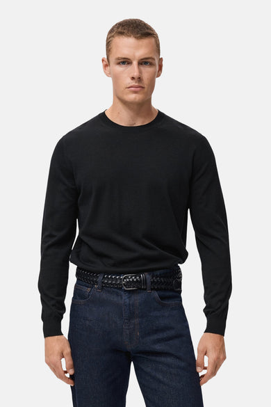 Zwarte rondehals trui van MANGO, gedragen met een donkere jeans en een gevlochten riem.