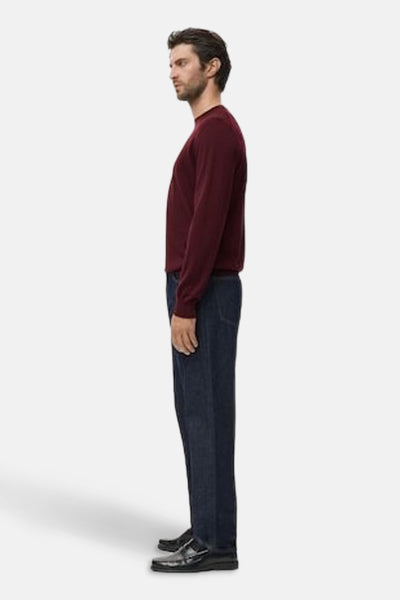 Bordeaux rondehals trui van MANGO, gedragen met een donkerblauwe broek en zwarte loafers, zijwaarts gezien.