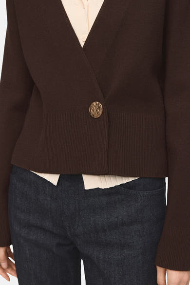Gilet marron par MANGO, avec un bouton texturé doré et une finition côtelée à la taille, porté avec un chemisier crème et un jean foncé.