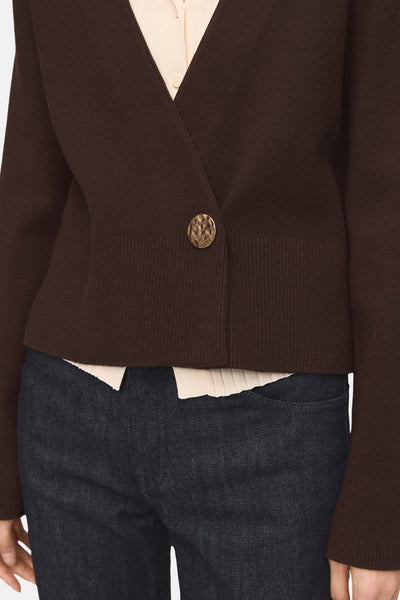 Gilet marron par MANGO, avec un bouton texturé doré et une finition côtelée à la taille, porté avec un chemisier crème et un jean foncé.